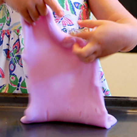 Kid playing with smooshy slime over a baking sheet.