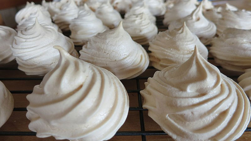 Cooling rack containing a bunch of swirly top meringues.