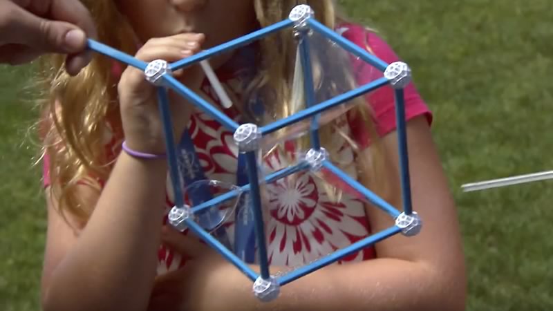Closeup of kids making square bubbles with a cube made out of straws.